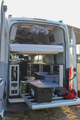 Inside an RV rental camper van, revealing a raised bed, organized storage, and a pull-out cargo platform with bins.
