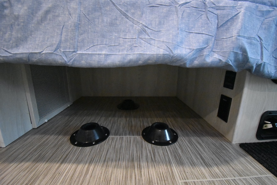 An RV rental's under-bed area has floor mounts for flexible furniture, power outlets, and a vent.