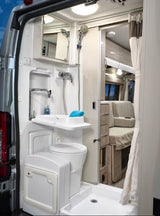 Inside an rv rental: a modern wet bath featuring a shower, toilet, and collapsible sink, with the living space beyond.