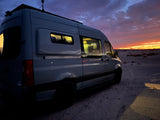 RV rental van parked at stunning desert sunset, interior lit, a person visible inside. Epic van life adventure.