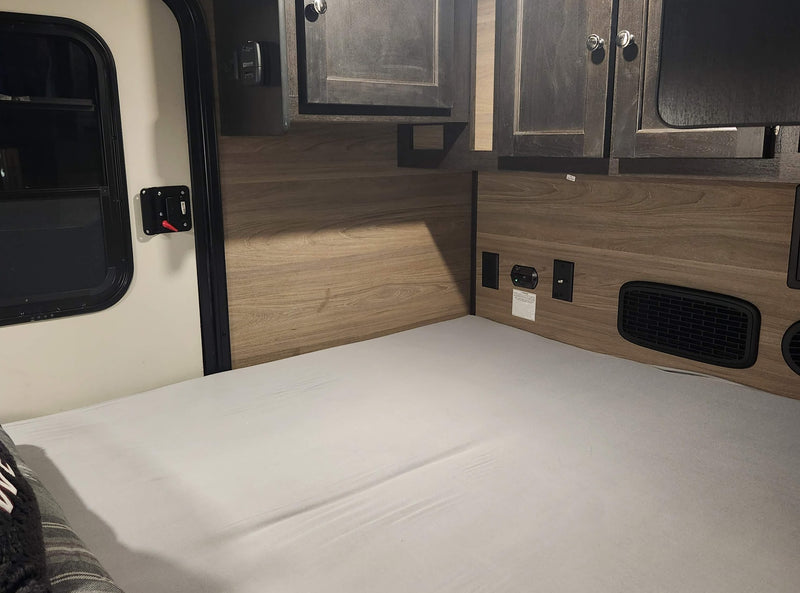 RV rental interior: cozy bed, wood walls with outlets/vents, and dark overhead cabinets by the door. — photo 5
