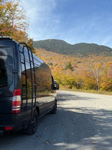 RV rental van parked on a gravel road with a scenic fall mountain backdrop and vibrant autumn foliage under a blue sky.