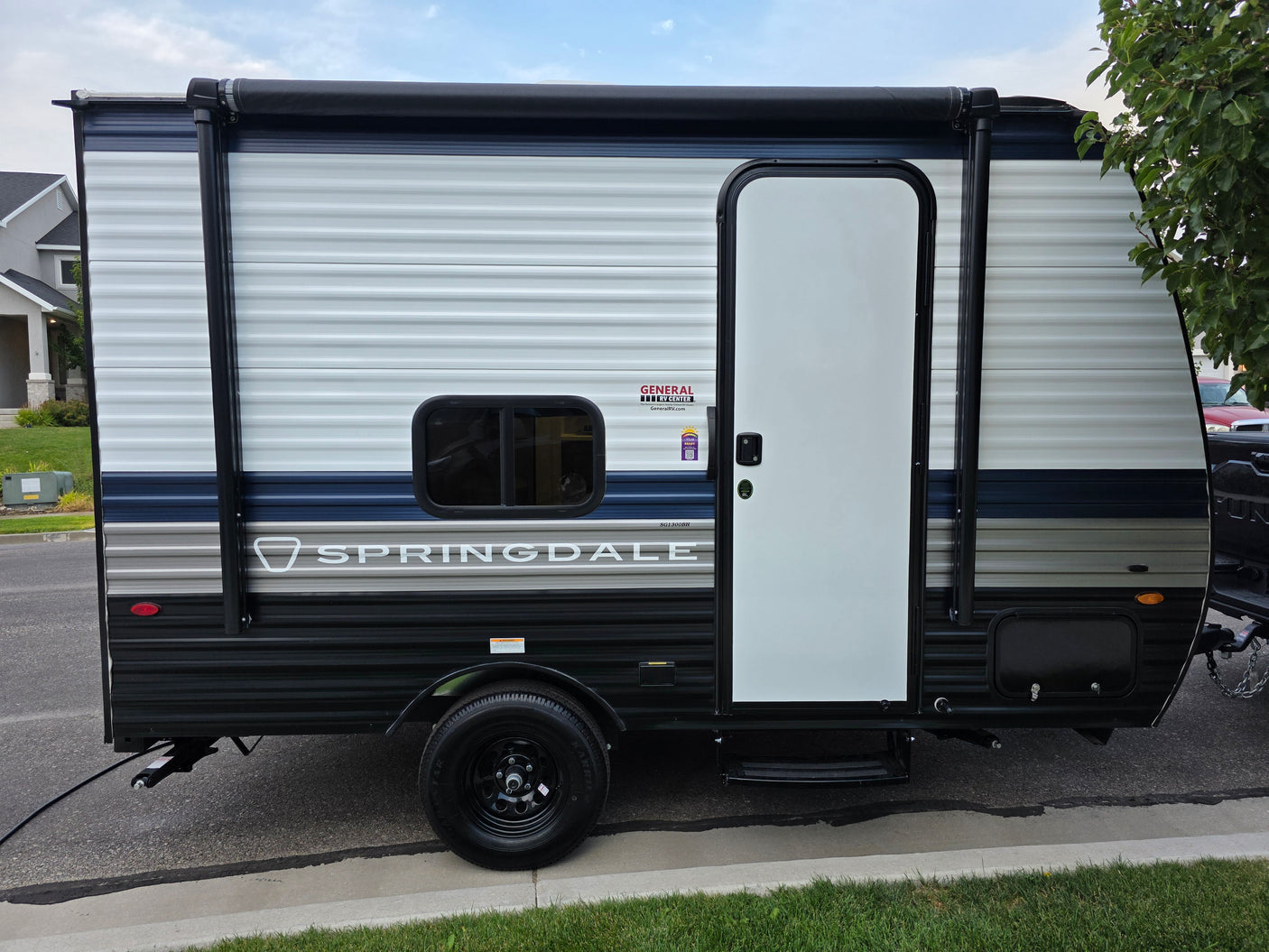 Springdale travel trailer for rv rental. Side view of a white, blue, & black RV parked on the street with an awning.