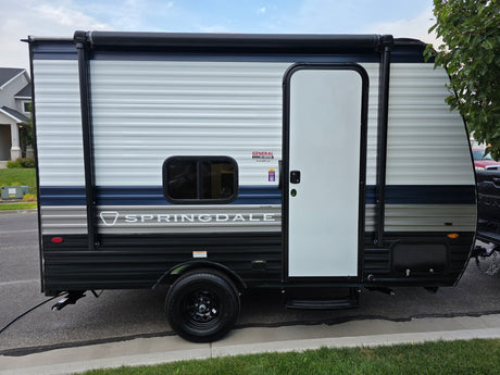 Springdale travel trailer for rv rental. Side view of a white, blue, & black RV parked on the street with an awning.