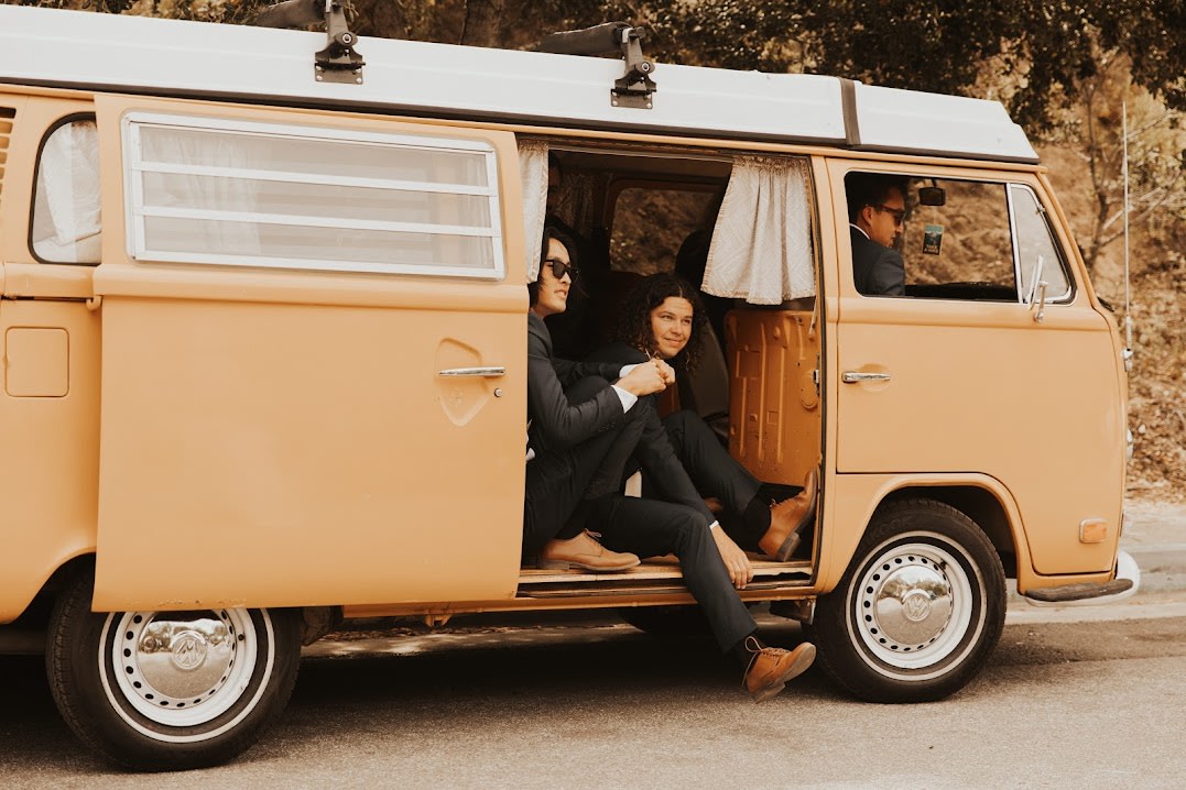 Three men in suits relax in a vintage orange VW camper van with the side door open, hinting at an RV rental adventure. — photo 5