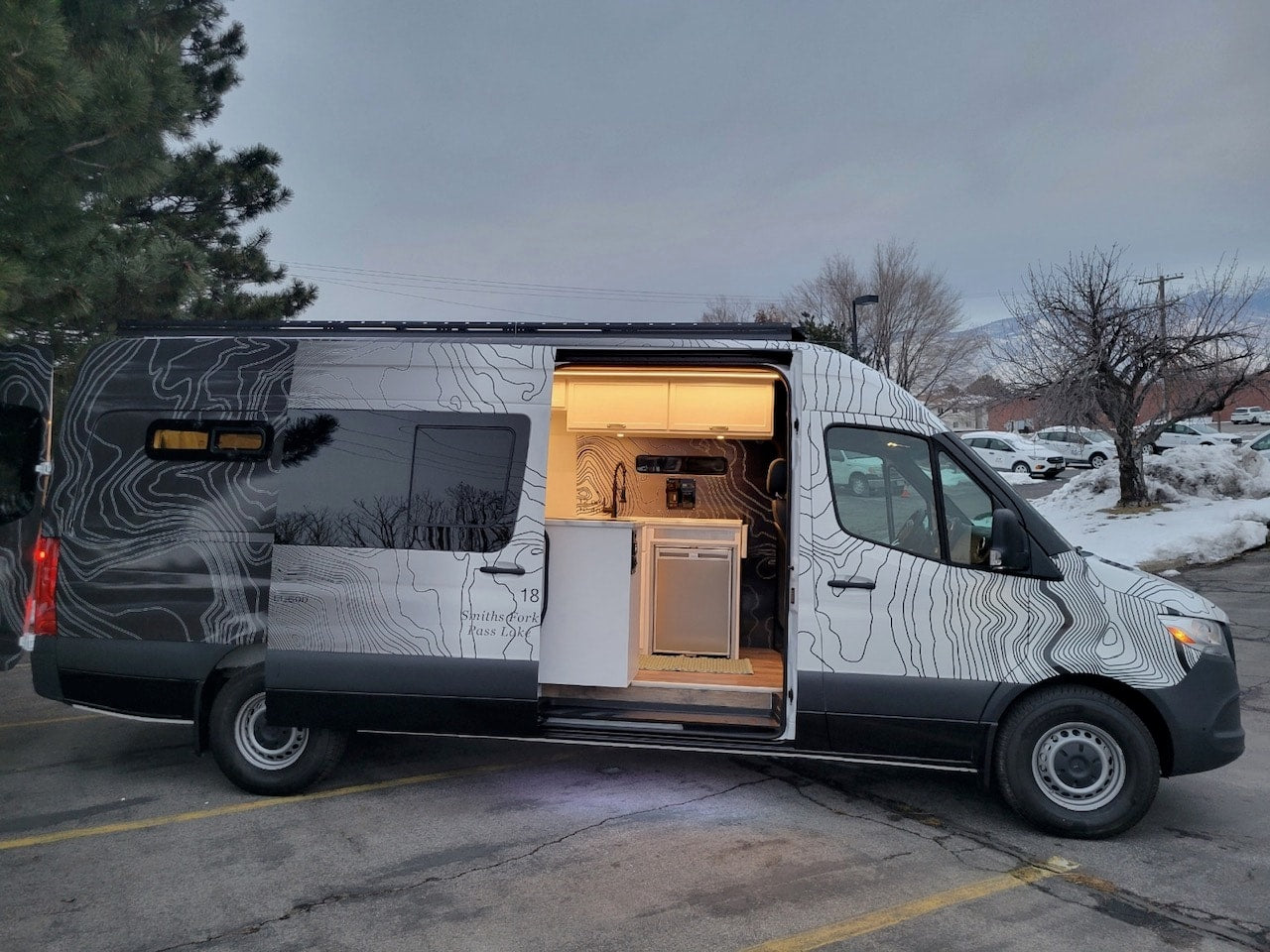 Custom van RV rental with open side door revealing a mobile kitchen, cabinets & unique topographical map design. — photo 10