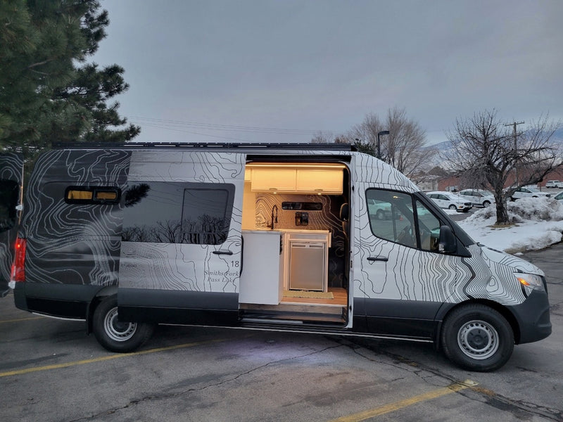 Custom van RV rental with open side door revealing a mobile kitchen, cabinets & unique topographical map design. — photo 10