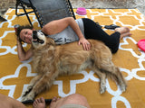 Smiling woman and her golden retriever relaxing on an outdoor mat, enjoying an RV rental getaway.