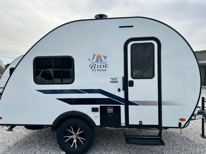 Side view of a white Braxton Creek 15DS travel trailer for RV rental, featuring the "Joy Ride" logo. — photo 1