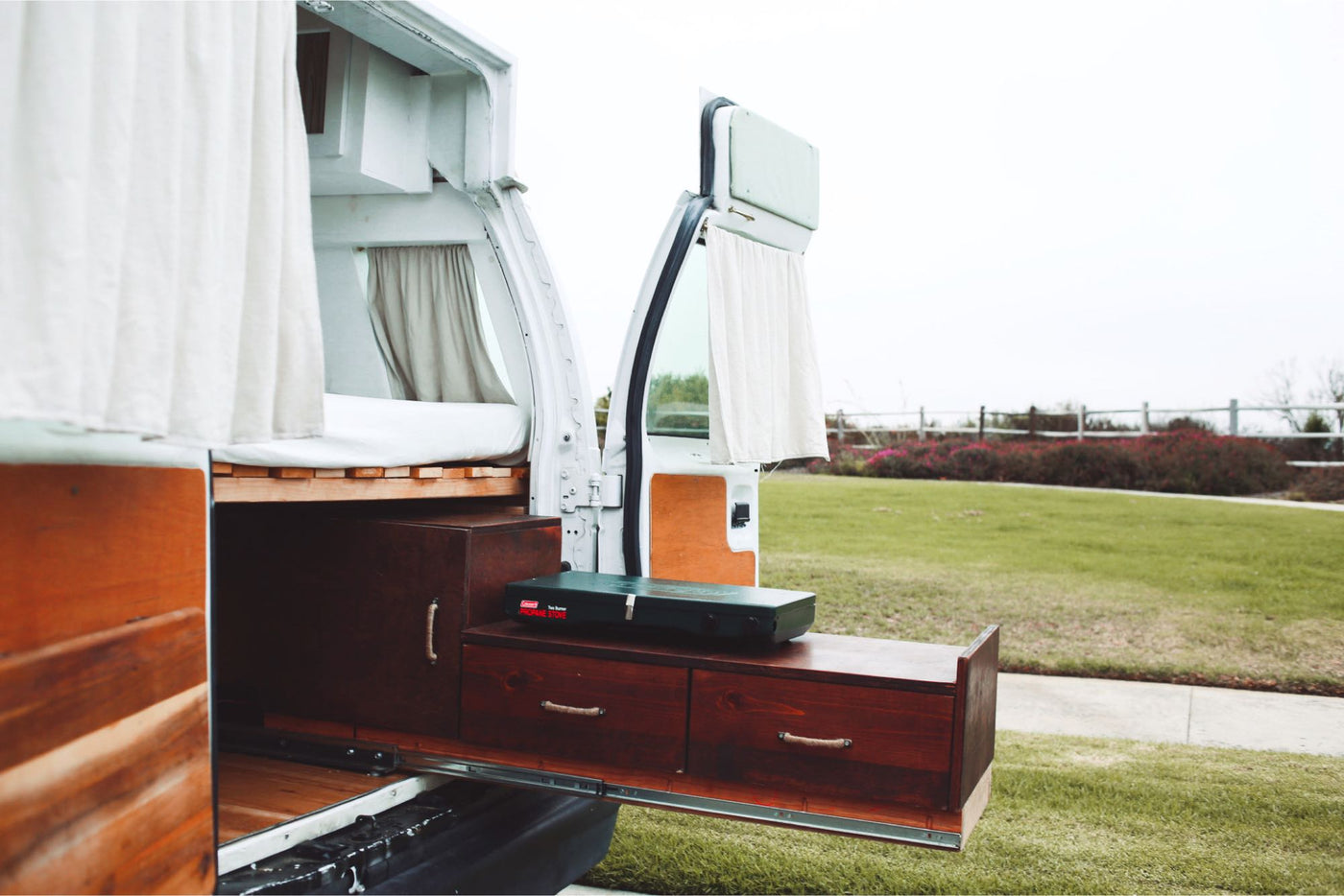Inside an **rv rental**: a white camper van with a wooden pull-out kitchen, Coleman stove, and bed, set for outdoor adventures. — photo 13