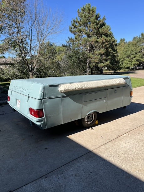 Light blue Coleman pop-up camper RV rental on a driveway, ready for camping. Classic travel trailer fun.