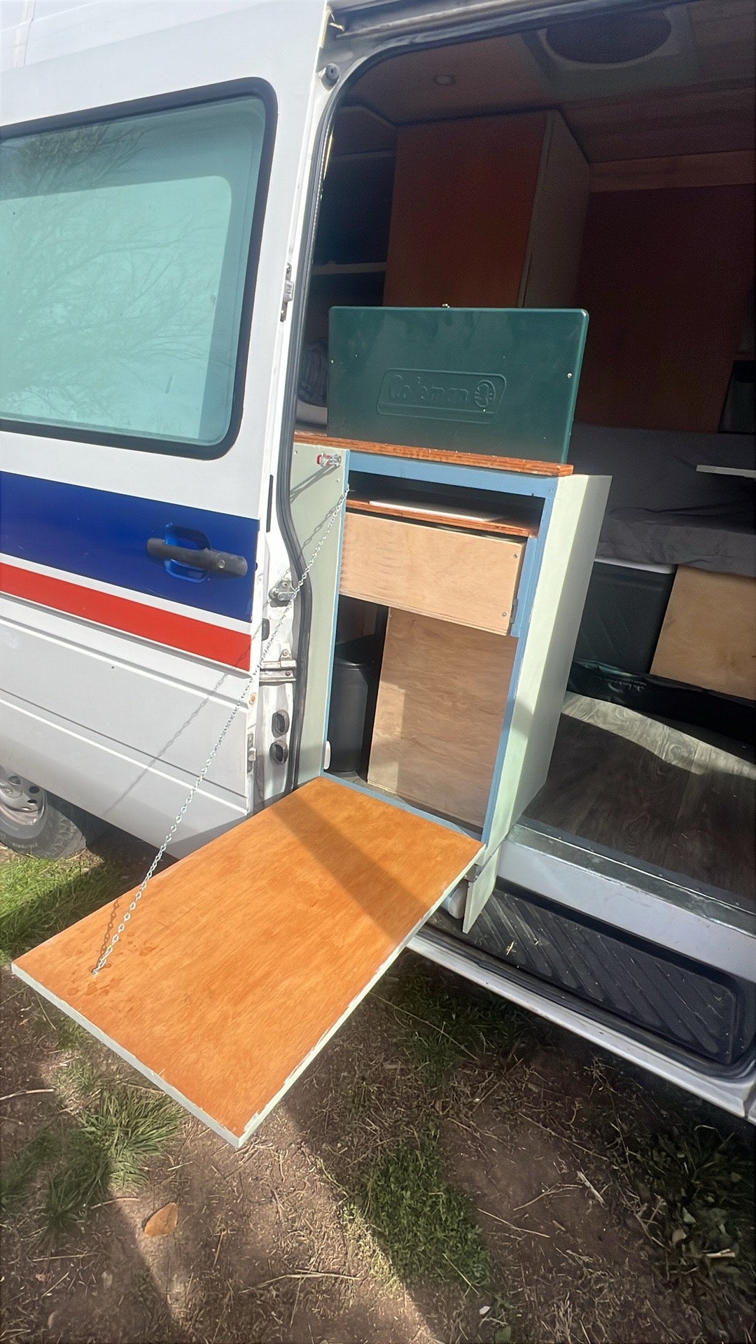 This **rv rental** features a van's custom outdoor kitchen: a fold-down table, Coleman stove, and storage. — photo 4