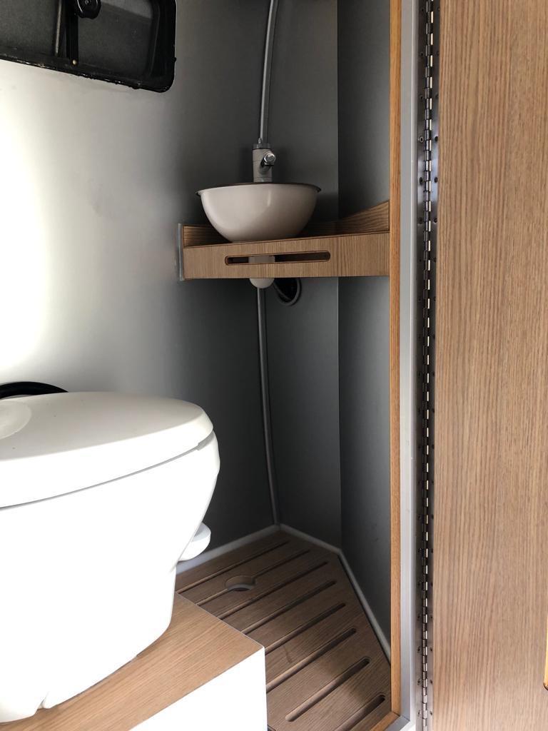Compact RV rental wet bath features a toilet, bowl sink on a wood shelf, and shower. Efficient, space-saving design. — photo 8