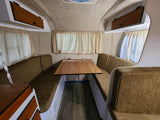 Inside a compact rv rental dinette with brown benches, wooden table, light curtains, and overhead storage for a functional space.
