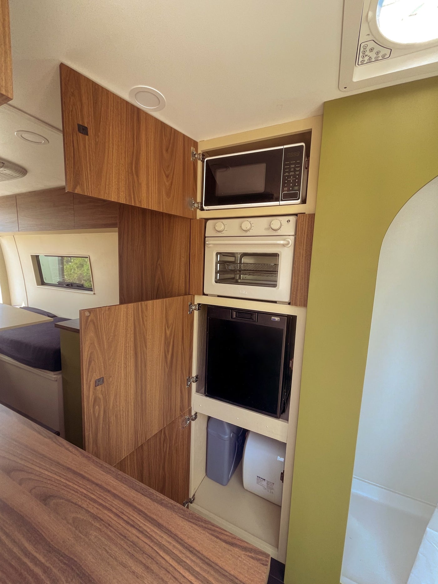 Modern RV rental interior: compact kitchenette featuring a microwave, oven, fridge, and lower storage. — photo 9