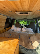 Cozy RV rental interior: a converted van with a natural wooden ceiling, a comfortable bed, and the front cabin visible.