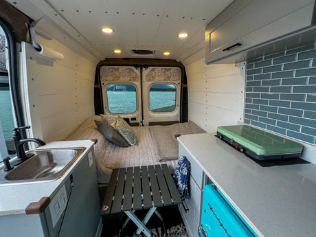 RV rental: Camper van interior features a cozy bed, compact kitchen, and scenic lake view from rear windows.