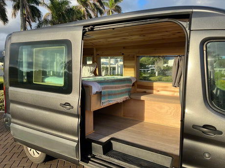 Gray rv rental camper van with open door revealing a custom wood interior, comfy bed, and bright windows for travel.