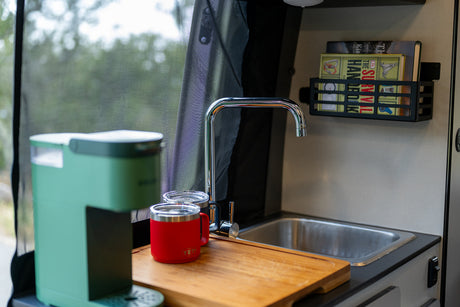 RV rental kitchen: green coffee maker, sink, YETI mug, and books. Perfect for cozy campervan adventures.