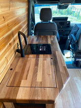 Modern RV rental interior with wood walls, sleek kitchen counter, sink, and induction cooktop. Perfect for camper van adventures!