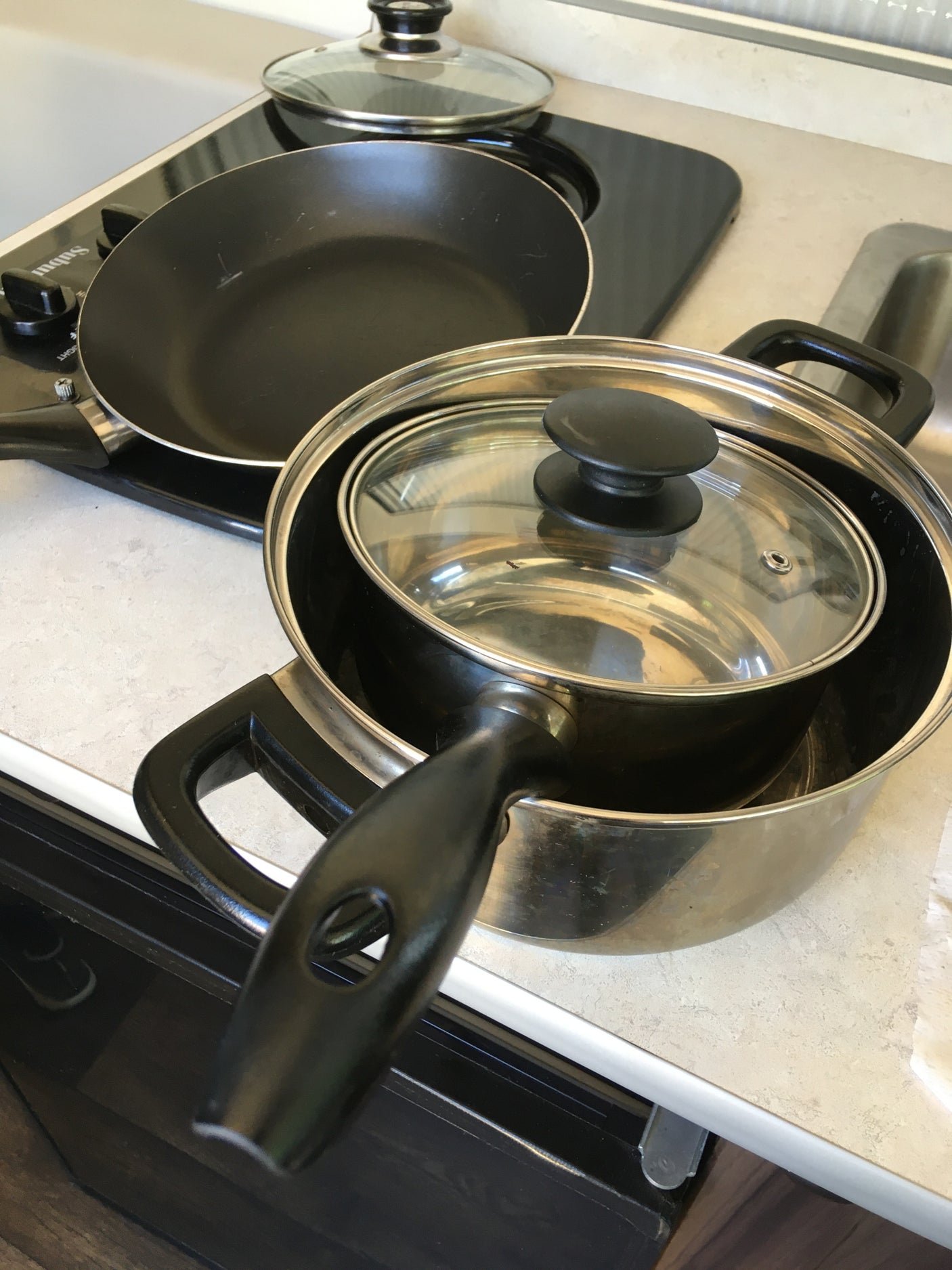 Compact RV rental kitchen featuring a cooktop with a frying pan and stacked pots for easy travel cooking.