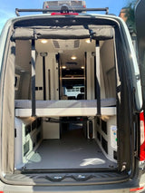 RV rental van interior from rear, showing a raised bed with spacious storage below. A clean, modern space for travel.