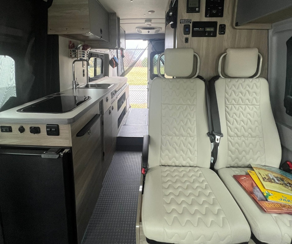 Clean RV rental interior featuring a functional kitchenette with a sink and stovetop, plus two comfortable passenger seats.