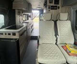Clean RV rental interior featuring a functional kitchenette with a sink and stovetop, plus two comfortable passenger seats.
