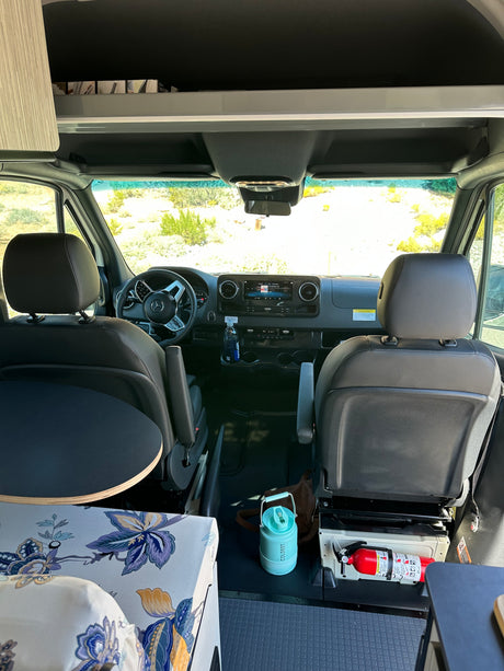 RV rental interior: View from the living area into the cockpit, showing front seats, dashboard, overhead storage, and a visible fire extinguisher.