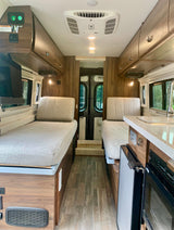 Bright RV rental interior with twin beds, a compact kitchen (sink, fridge, oven), and overhead storage.