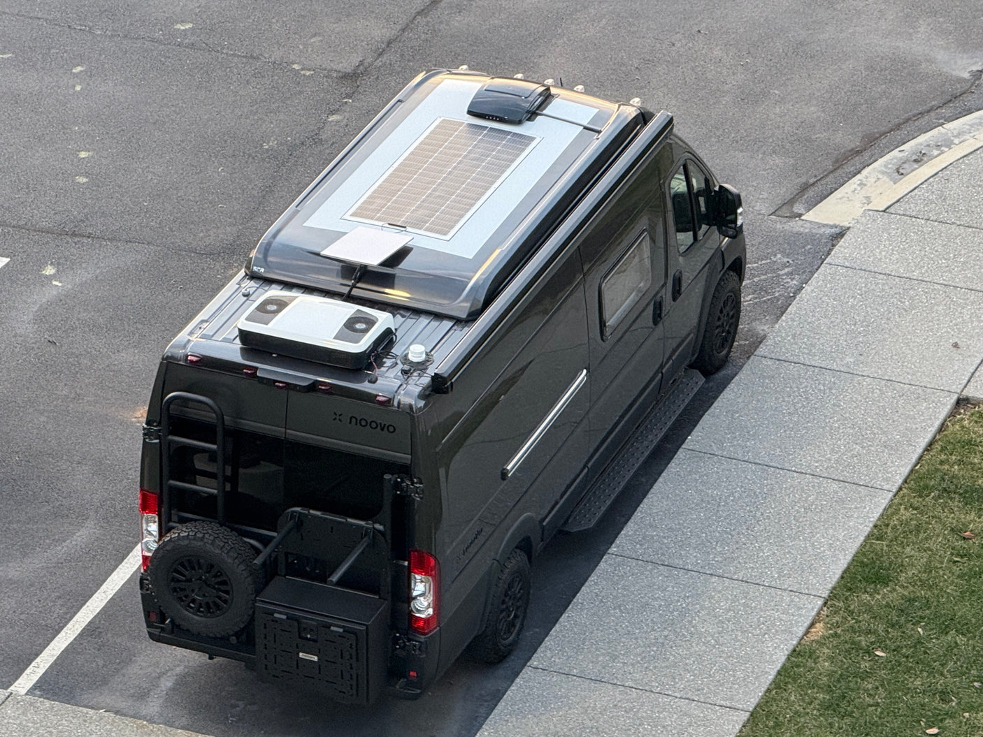 Sleek black Noovo RV rental, ready for adventure, featuring roof solar, ladder, and rear storage. Parked on asphalt.