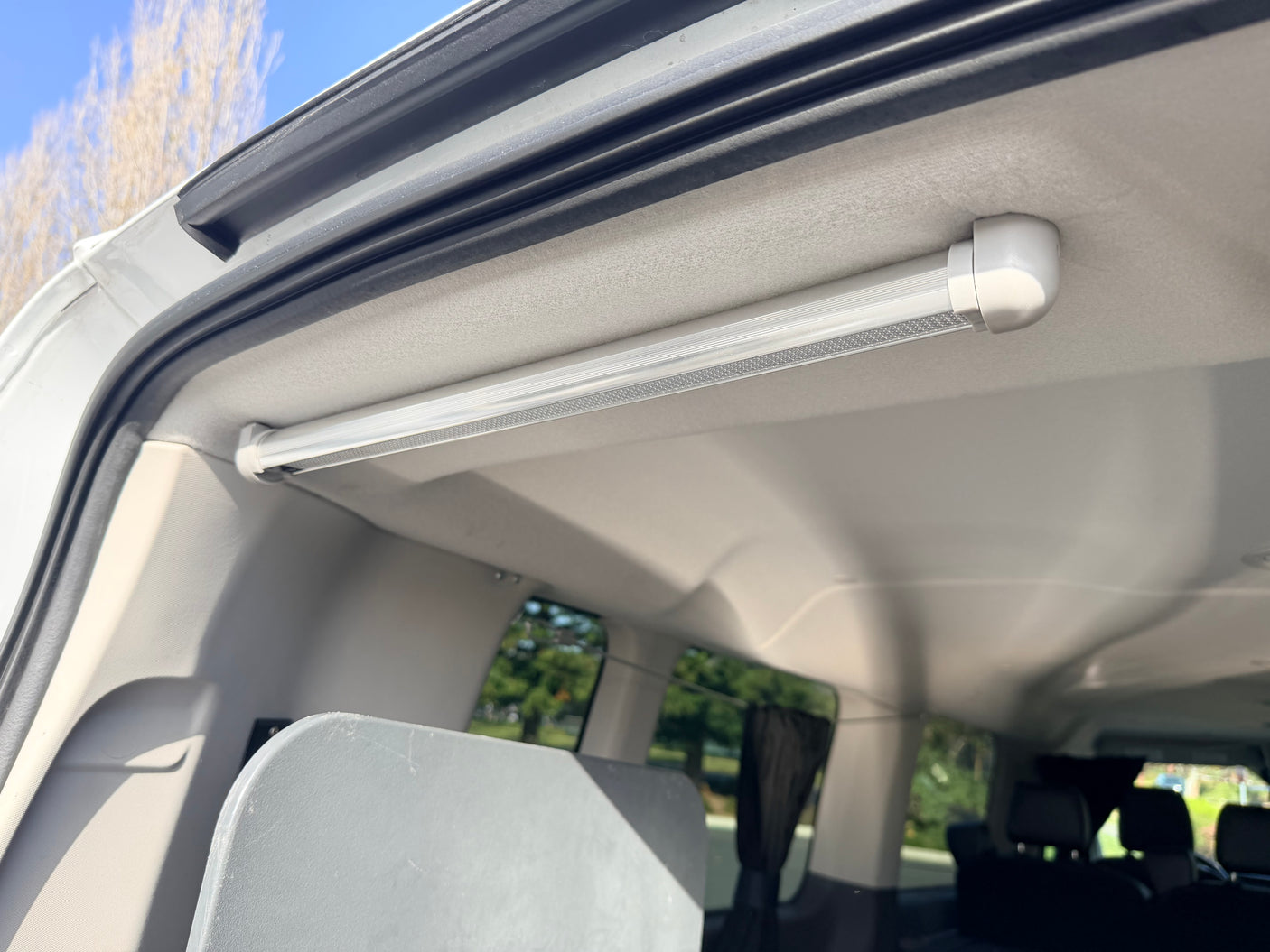 Inside an RV rental, a long LED ceiling light brightens the rear area. Upholstered ceiling, back seats, and outdoor view through windows.
