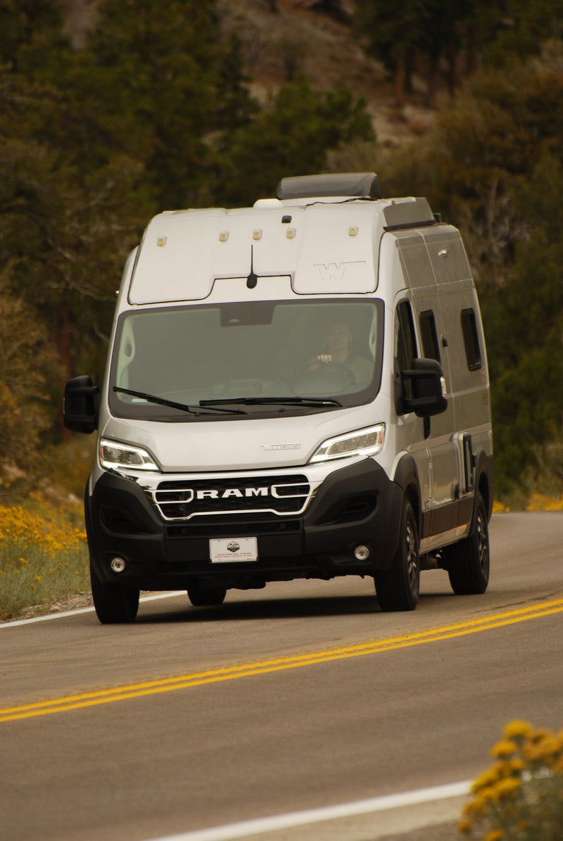  with tall plants & distant mountains under a blue sky.|Grey RV rental driving on a scenic mountain road — photo 8