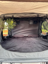 Comfortable rooftop tent interior, ideal for RV rental camping. Features soft bedding, pillows, and nature views through windows.