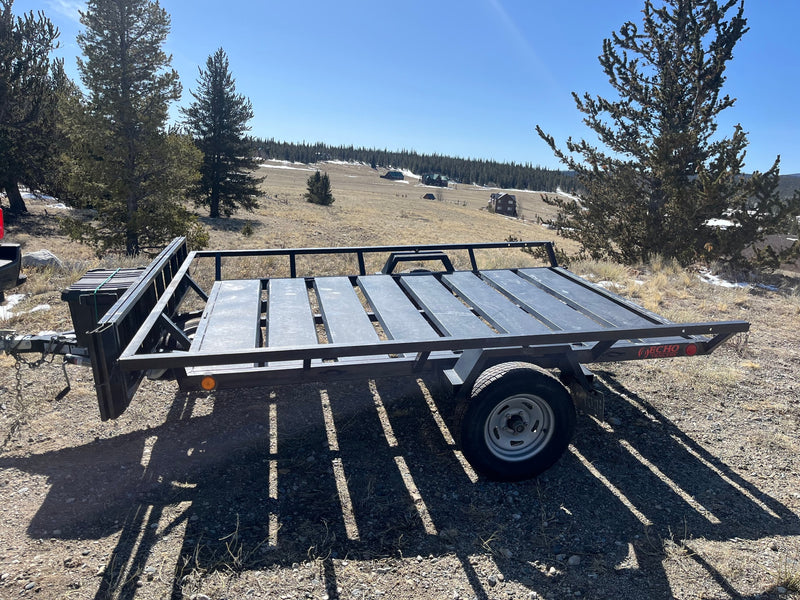 Black utility trailer in a sunny mountain landscape with pines & homes. Great for gear with an RV rental. — photo 3