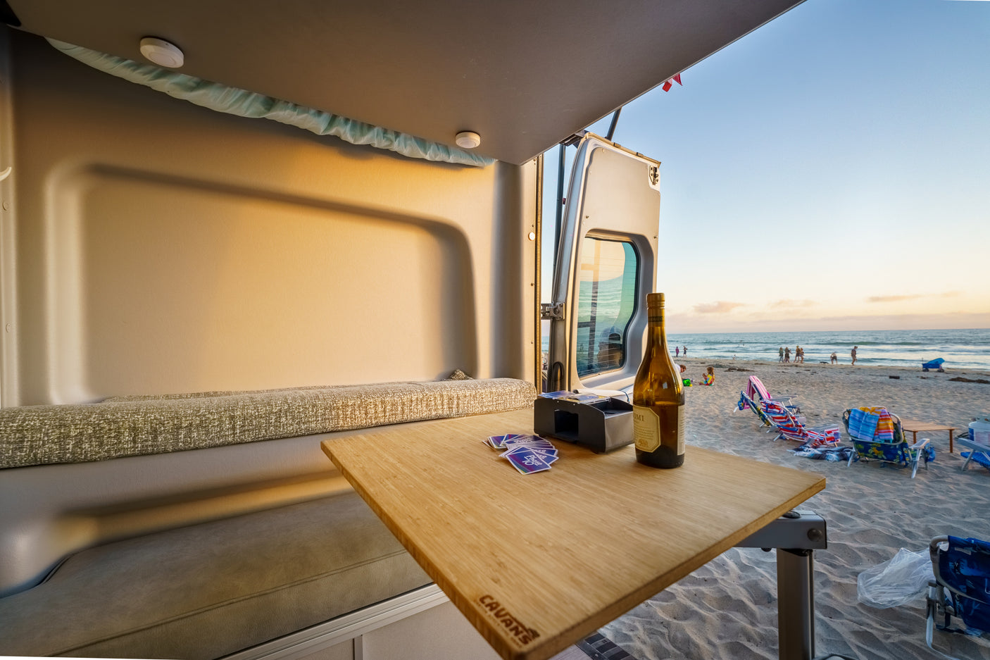 RV rental view: playing cards and enjoying wine from inside a camper van, overlooking a serene beach at sunset.