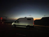 Scenic twilight view of an RV rental campervan parked by the ocean with distant mountains. Ready for adventure.