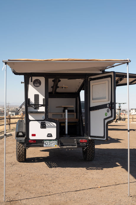 An open off-road TAXA camper with deployed awning, revealing its compact interior setup. Great for adventure or rv rental.