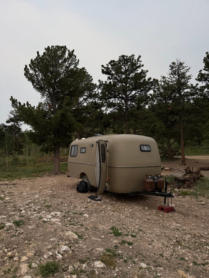  parked among pine trees on a rocky campsite.|Two men enjoy their rv rental interior. One takes a selfie in a cozy — photo 2