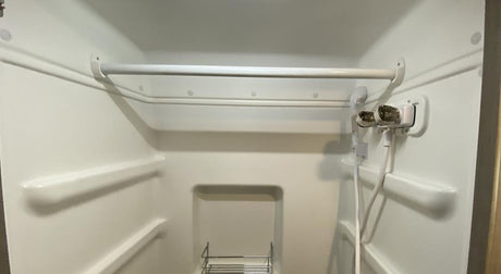 Step inside a typical RV rental shower: compact white unit with a handheld shower, built-in shelves, and a metal caddy.