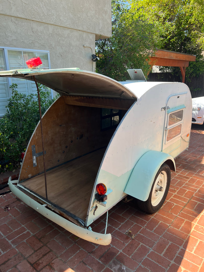 A small white and light green teardrop camper, an ideal RV rental, open at the rear, sits on brick pavers. — photo 3