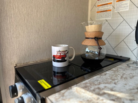 Inside an RV rental: a white mug with a red Jeep design & a Chemex coffee maker on a black cooktop.