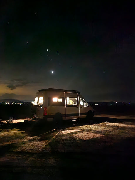 Cozy RV rental illuminated at night, parked with the moon and distant lights visible, ideal for peaceful camping.