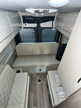 RV rental interior with modern diamond-stitched seating, light wood flooring, overhead storage, and rear windows.