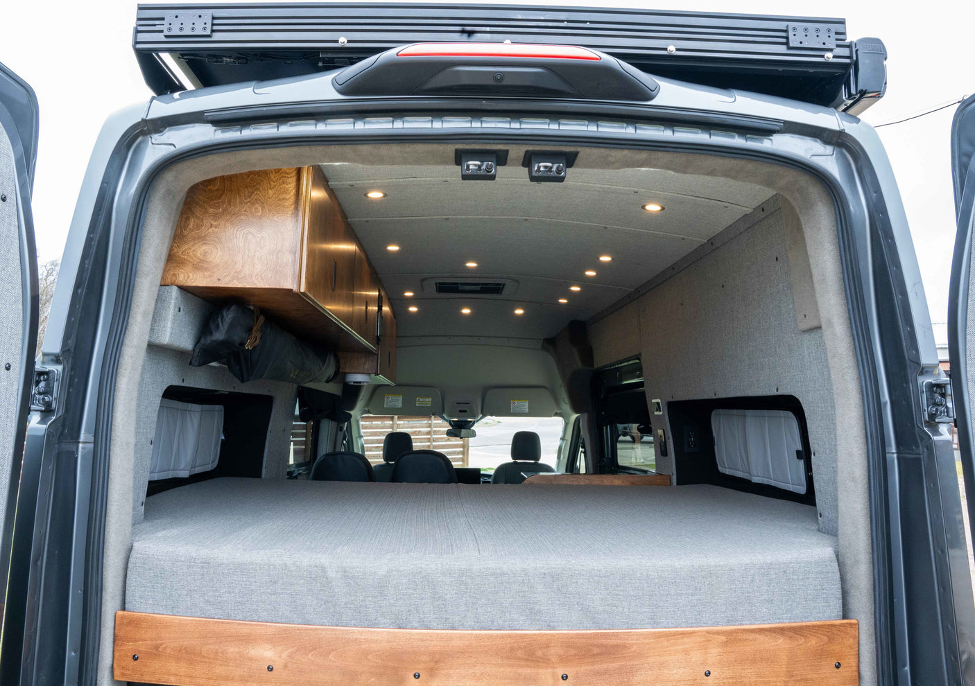 Inside a well-appointed rv rental camper van, featuring a comfy bed, wood cabinetry, and ambient ceiling lights.