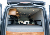 Inside a well-appointed rv rental camper van, featuring a comfy bed, wood cabinetry, and ambient ceiling lights.