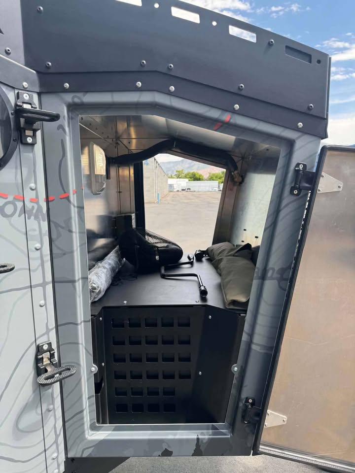 Cabin door of the XPedition Voyager Sky XE swung open, showing the padded sleeping platform, gear hammock and interior storage cabinet, with the topographic-map wrap on the door skin — photo 6