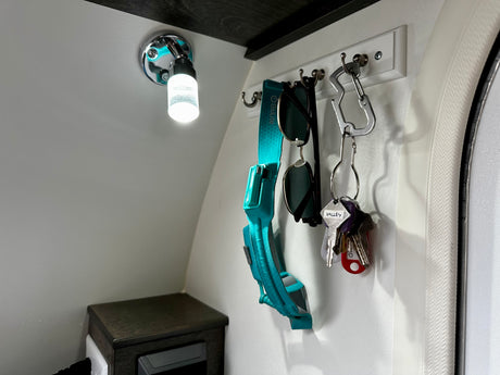 RV rental interior showing efficient organization: light, wall hooks with keys, sunglasses, and outdoor gear strap.