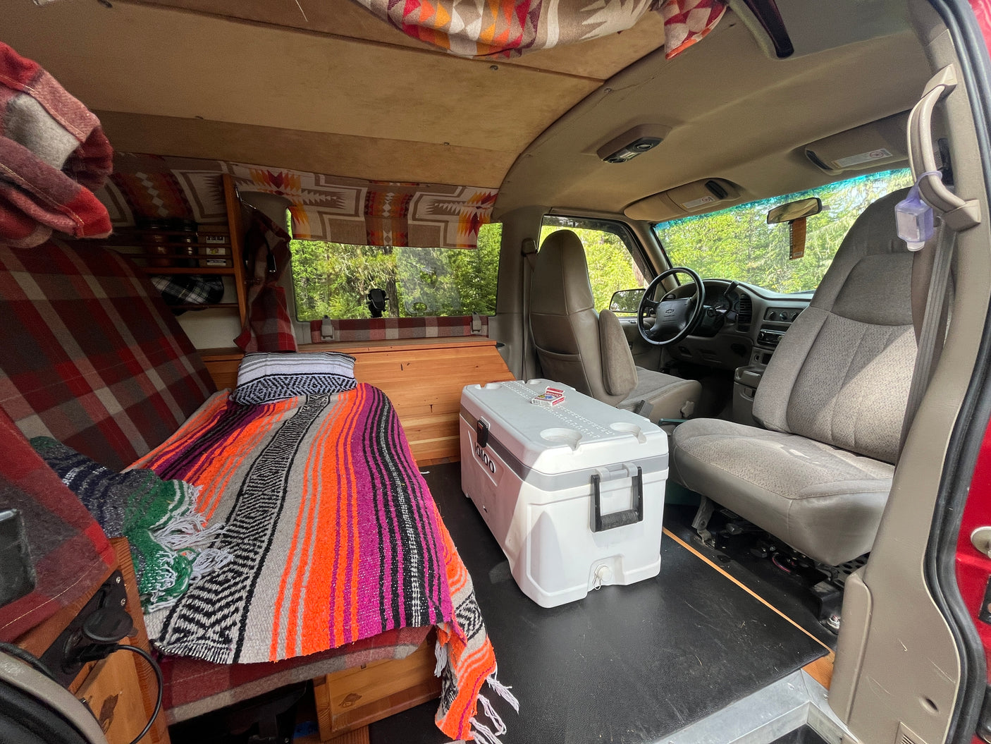 Cozy RV rental interior with a custom bed, Igloo cooler, and driver's area. Perfect for van life!