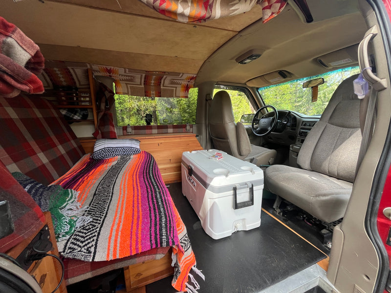 Cozy RV rental interior with a custom bed, Igloo cooler, and driver's area. Perfect for van life! — photo 6